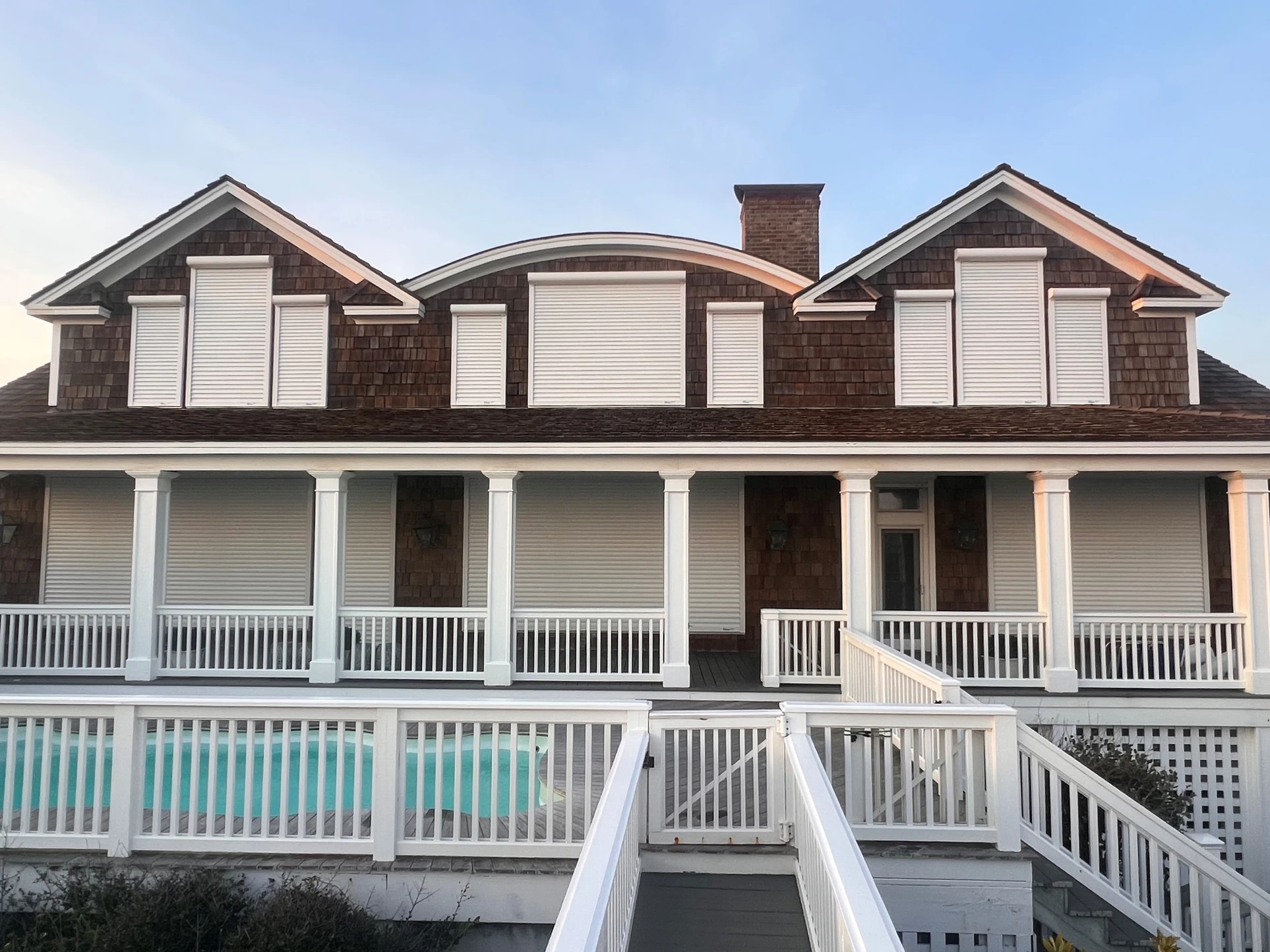 661c5d_07f97d5063ab40cbb7fa68a54cc3bd7b~mv2 Two-story house with closed white storm shutters and a white railing, overlooking a pool—ideal for North Carolina’s weather.