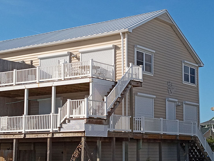 Beige elevated house with white railings, exterior stairs, and closed storm shutters on windows and doors for storm protection in Morehead City, North Carolina.