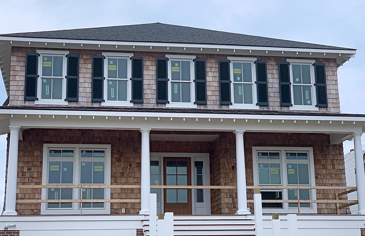 661c5d_4c14d3c9944849b98cc1fcf9b Two-story house in North Carolina with brown shingles, black shutters, white trim, storm protection features, and a covered front porch.