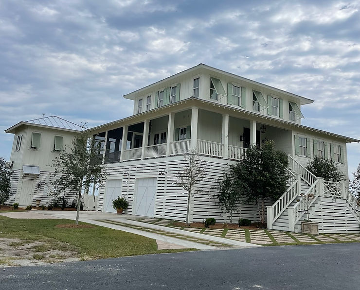 661c5d_8ab55282426f404db16d6b784 Large white two-story beach house with storm shutters and a wraparound porch, offering storm protection under a cloudy sky in Morehead City.