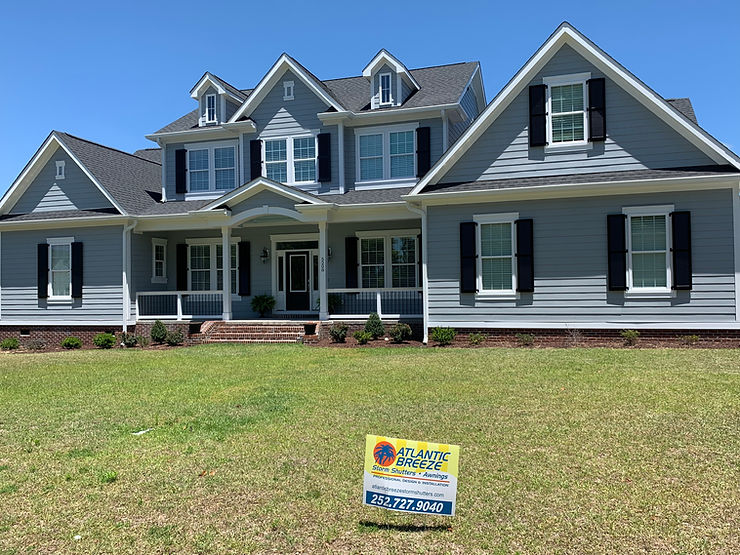 661c5d_b49c0dbb15a941a19bd73f3b9 Large gray house with white trim in Morehead City, featuring a yard sign for Atlantic Breeze, a cleaning and restoration service.