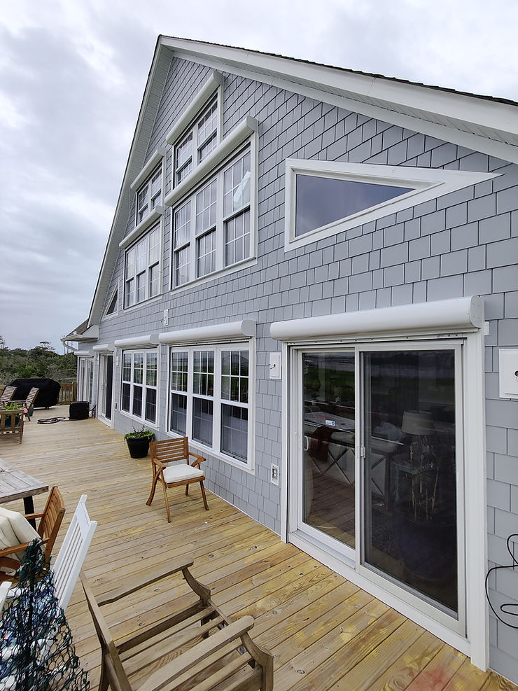 Modern house with gray siding and many windows, shown from a wooden deck with outdoor furniture—perfect for enjoying North Carolina views and built with storm protection in mind.
