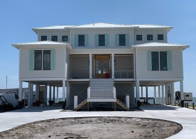 A large, elevated coastal house with pale blue storm shutters and a central staircase stands under a clear sky, capturing the essence of Atlantic Breeze.