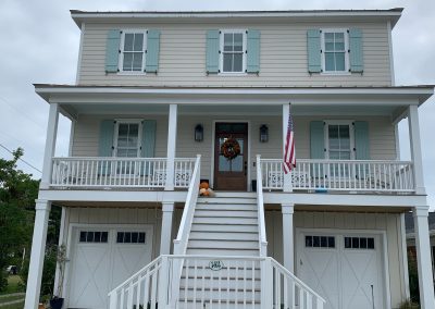 Two-story beige house with blue storm shutters, front porch, pumpkins on steps, and an American flag—perfect for charming storm protection in Morehead City.