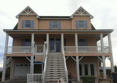 Two-story peach house with blue shutters, white trim, and a large front staircase leading to the porch—perfect for enjoying the Atlantic Breeze in Morehead City.