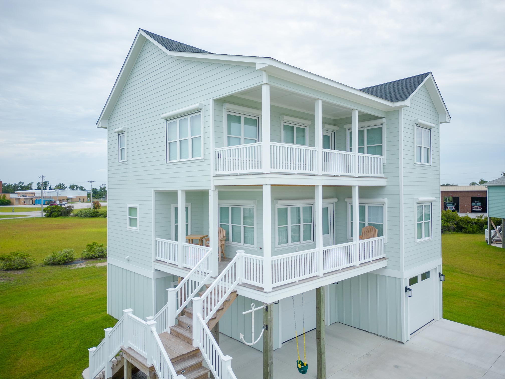 Atlantic-Breeze-0888 Hurricane Protection Products: Light blue two-story house on stilts with white railings and a wraparound porch.