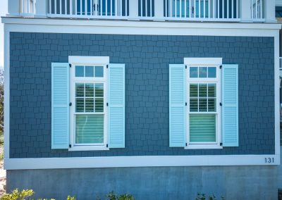 Two white-shuttered windows on a blue house exterior with a white trim and house number 131 offer classic charm and Atlantic Breeze-inspired storm protection.