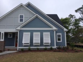 Blue house with white storm shutters closed on the windows and a small front yard with mulch and grass, located in Morehead City, North Carolina.