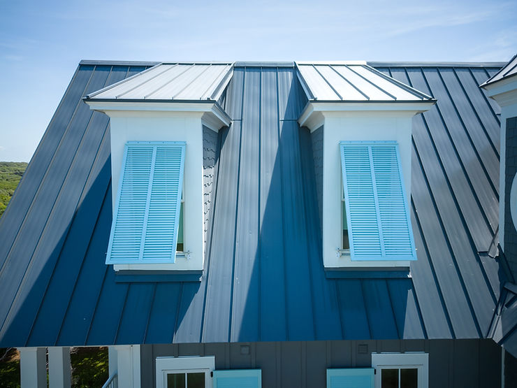 ebbd78_6f5747077b5049c1841013d7e Blue metal roof with two dormer windows, each with closed light blue shutters, under a clear Morehead City sky in North Carolina.