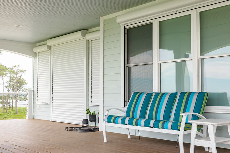 ebbd78_789480a37b0b47369be5f5b7e Striped blue and green bench on a porch in Morehead City, featuring closed white roll shutters for added storm protection and a wooden floor.