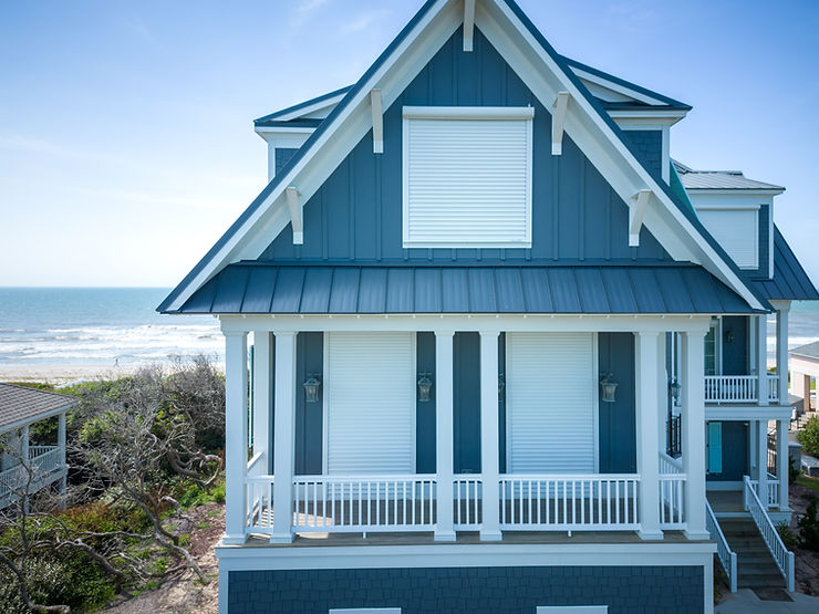 Blue beach house with closed storm shutters, facing the ocean under a clear blue sky—classic Atlantic Breeze charm in North Carolina.