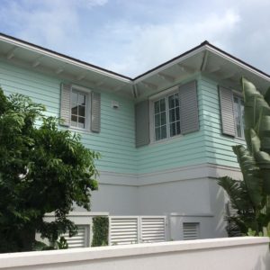 A mint green house with white trim, gray storm shutters, and lush tropical plants in front captures the Atlantic Breeze of Morehead City.