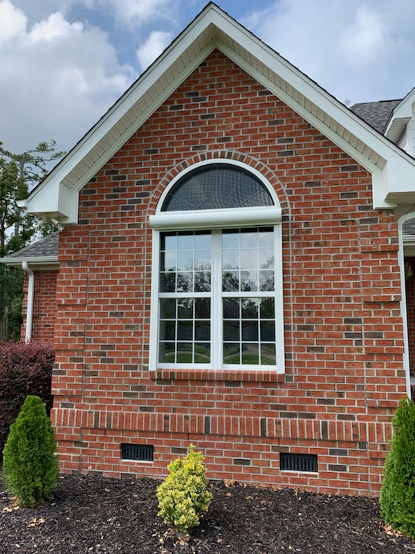 Brick house with a large arched window, white trim, and small bushes in front landscaping offers reliable storm protection with durable storm shutters—perfect for Morehead City’s weather.