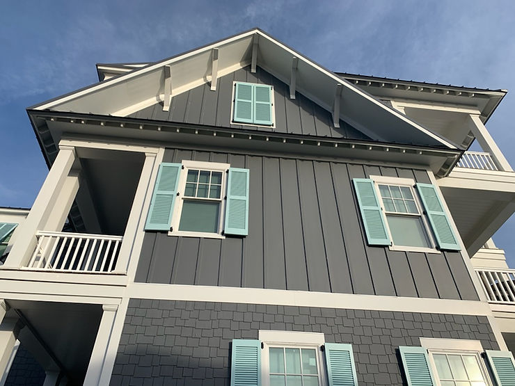 Gray house with teal storm shutters and white trim, viewed from below against a blue sky, adding both charm and storm protection.