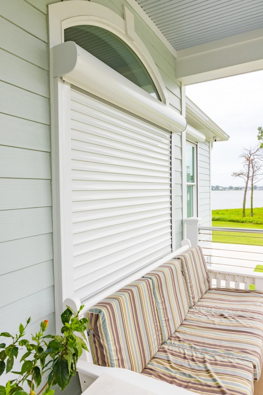 single qmi Striped cushioned bench on a porch next to a window with a closed white rolling shutter.