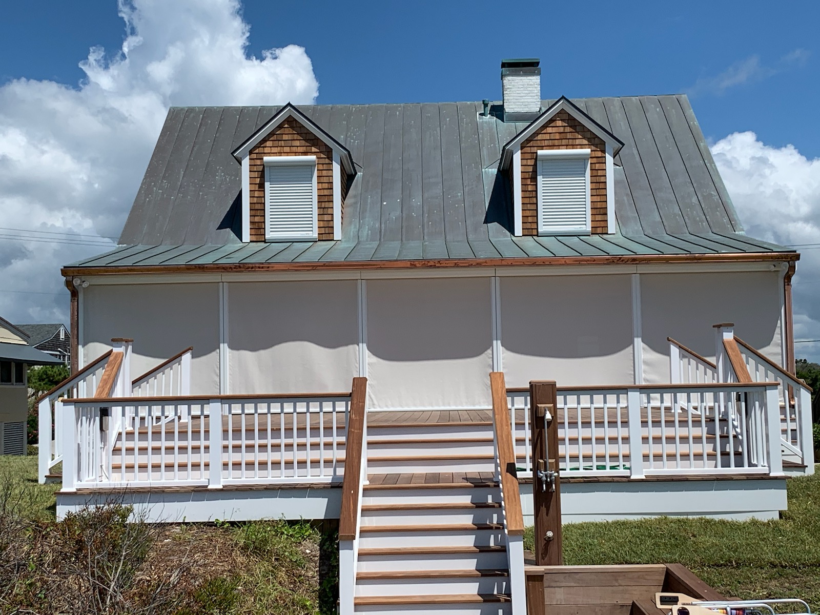 ATLANTIC-BREEZE-STORM-SHUTTERS-WIND-SCREENS6 A white house with a metal roof, two dormer windows, and a front porch with stairs and railings.
