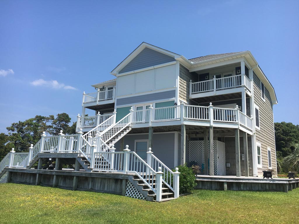 Large two-story beach house with multiple balconies and white railings under a clear blue sky.
